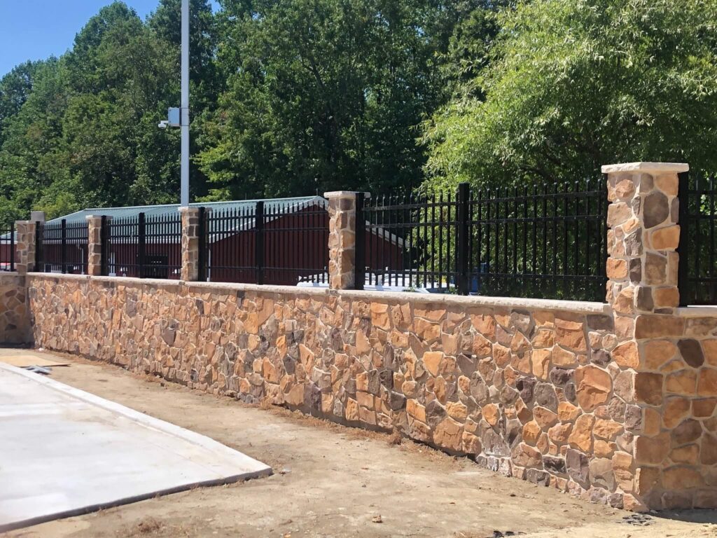 a stone wall and fence in front of a parking lot